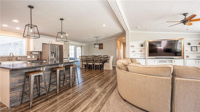 living area with ceiling fan, vaulted ceiling, wood finished floors, and ornamental molding