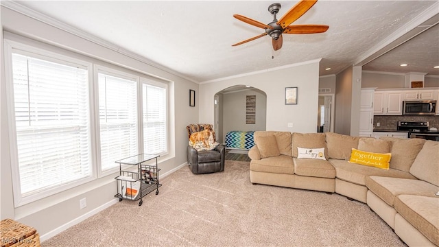 carpeted living room with ceiling fan, baseboards, arched walkways, and ornamental molding