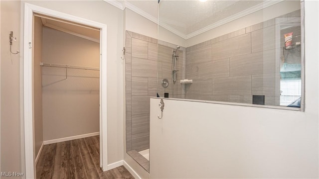 bathroom featuring wood finished floors, baseboards, ornamental molding, a walk in shower, and a walk in closet