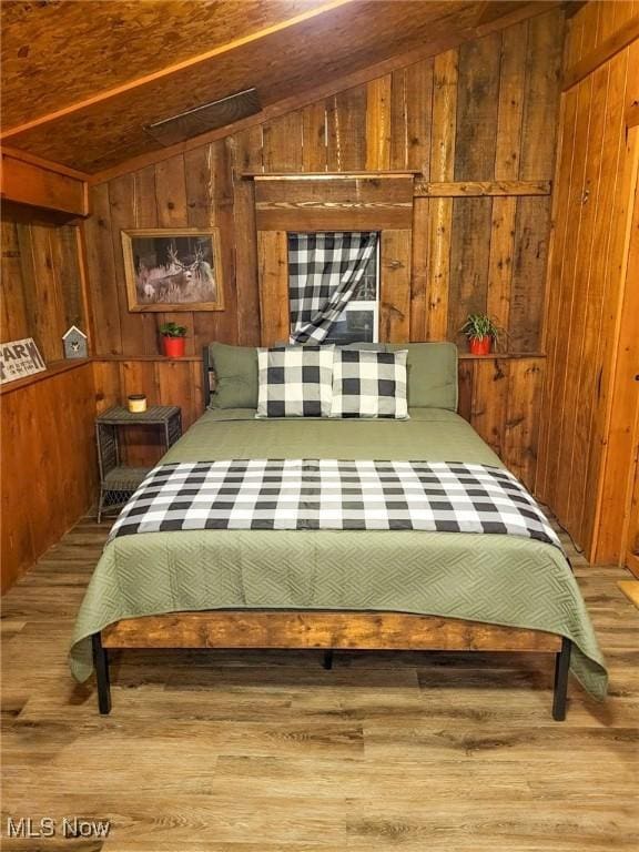 bedroom with wood walls, wood finished floors, and vaulted ceiling