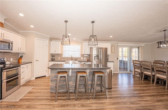 kitchen with dark countertops, ornamental molding, light wood-style flooring, appliances with stainless steel finishes, and a sink