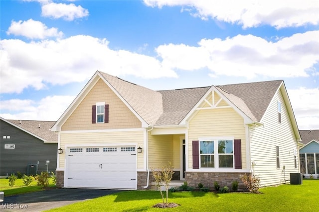 craftsman-style house featuring central air condition unit, a front yard, a garage, stone siding, and driveway