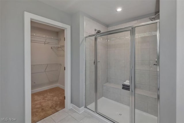 full bath featuring tile patterned floors, a shower stall, a walk in closet, and baseboards