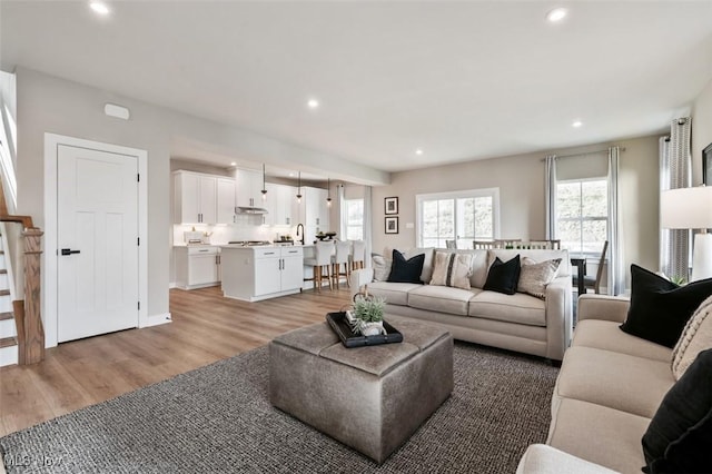 living area with recessed lighting, light wood-type flooring, baseboards, and stairway