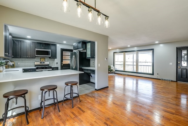 kitchen featuring a sink, backsplash, appliances with stainless steel finishes, light wood finished floors, and light countertops