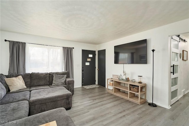 living room with a barn door, wood finished floors, and baseboards