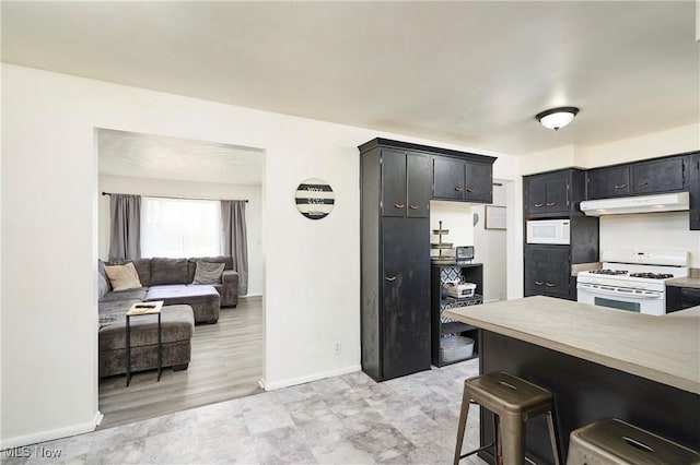 kitchen featuring white appliances, a breakfast bar, light countertops, under cabinet range hood, and dark cabinets