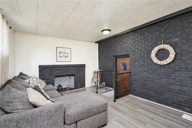 living room with a brick fireplace, wood finished floors, and brick wall