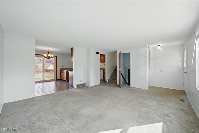 unfurnished living room featuring stairs, a notable chandelier, carpet, and visible vents