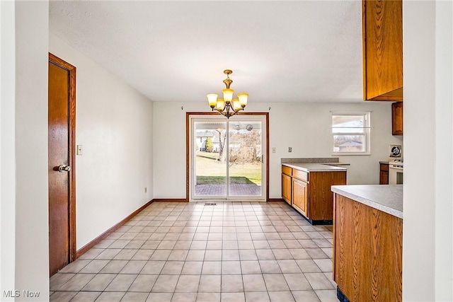 kitchen featuring light tile patterned floors, brown cabinetry, baseboards, light countertops, and a notable chandelier