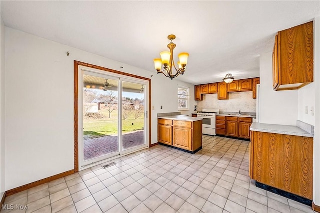 kitchen with light countertops, white range with gas cooktop, brown cabinets, a peninsula, and a notable chandelier