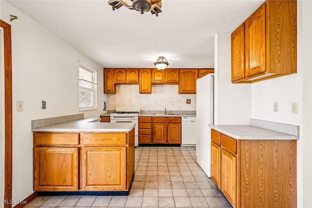 kitchen featuring a sink, white appliances, a peninsula, brown cabinetry, and light countertops