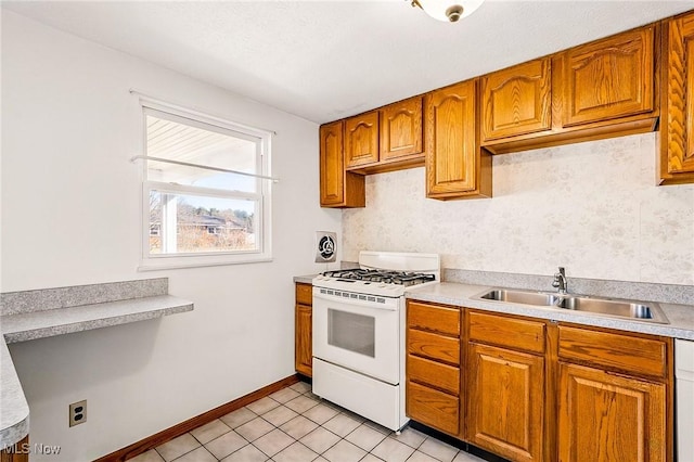 kitchen featuring a sink, white range with gas cooktop, brown cabinets, and light countertops