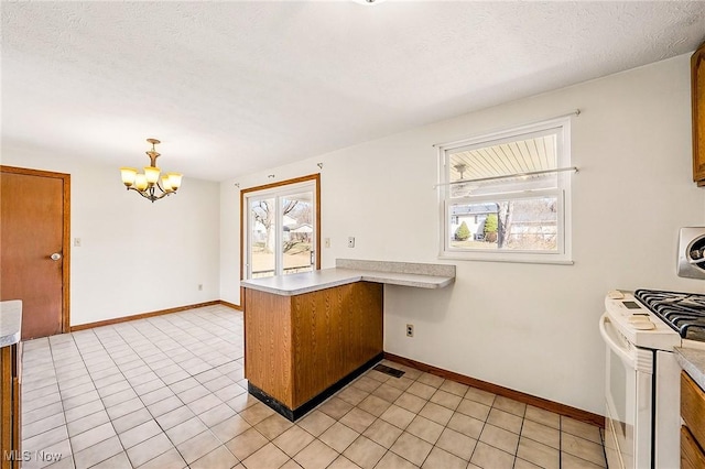 kitchen featuring brown cabinets, white gas stove, a peninsula, light countertops, and a chandelier