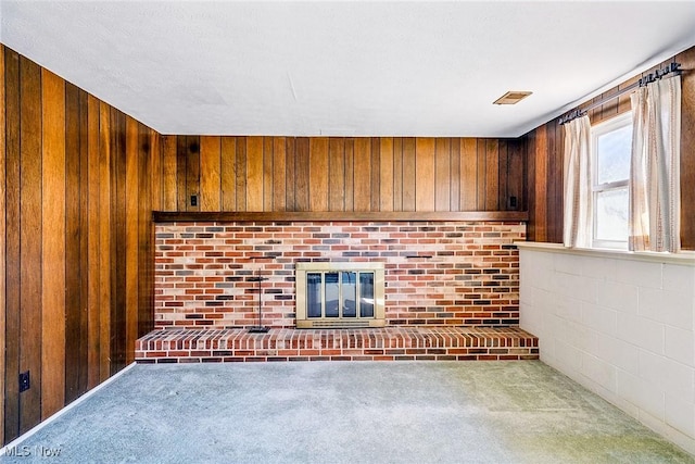 unfurnished living room with wooden walls, a fireplace, and carpet