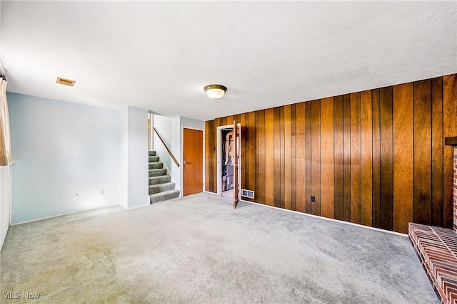 carpeted spare room featuring stairway, wood walls, and visible vents