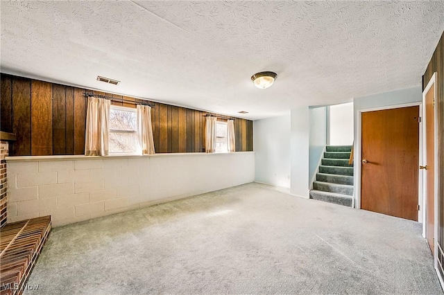 below grade area with visible vents, stairs, carpet flooring, a textured ceiling, and concrete block wall