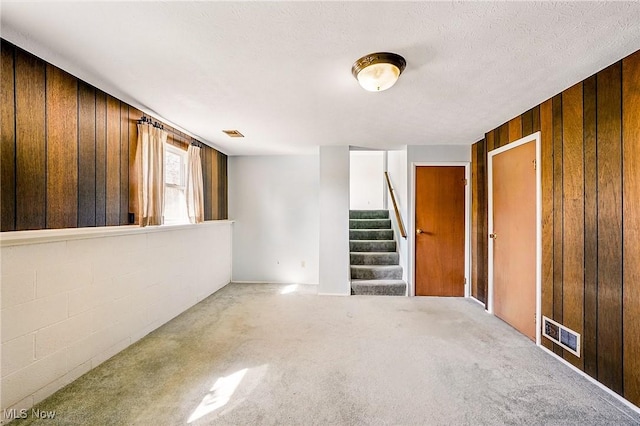 unfurnished room featuring stairway, carpet, visible vents, wood walls, and a textured ceiling