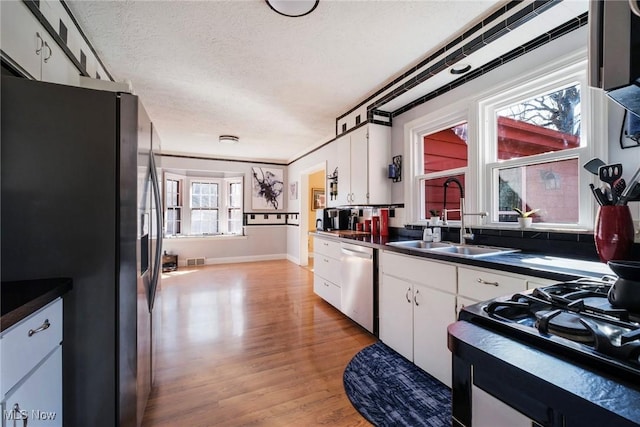 kitchen featuring a sink, dark countertops, appliances with stainless steel finishes, white cabinets, and light wood finished floors