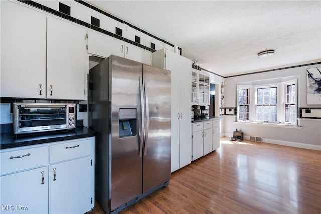 kitchen with dark countertops, visible vents, stainless steel refrigerator with ice dispenser, and a textured ceiling