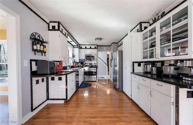 kitchen with light wood-style flooring, a sink, white cabinets, appliances with stainless steel finishes, and dark countertops