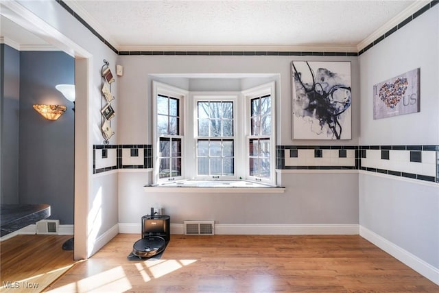 interior space with visible vents, a textured ceiling, wood finished floors, and crown molding