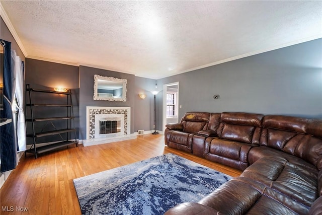 living area with crown molding, baseboards, a tiled fireplace, wood finished floors, and a textured ceiling