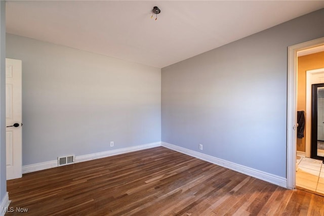 spare room featuring wood finished floors, visible vents, and baseboards