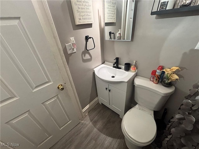 half bathroom featuring baseboards, toilet, wood finished floors, and vanity