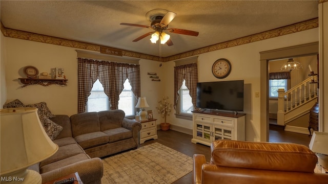 living area with baseboards, stairway, ceiling fan with notable chandelier, dark wood-style floors, and a textured ceiling