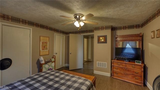 bedroom with visible vents, baseboards, a textured ceiling, and wood finished floors