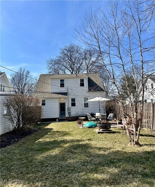 back of property with a fire pit, roof with shingles, a yard, and fence