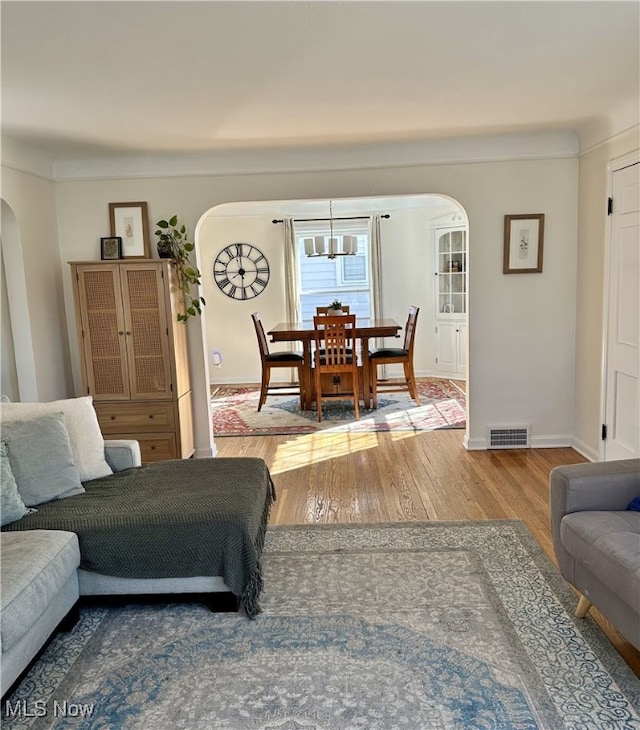 living room featuring visible vents, arched walkways, baseboards, and wood finished floors