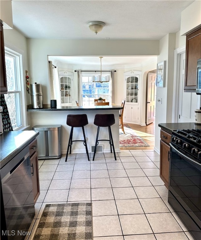 kitchen featuring light tile patterned floors, a breakfast bar, black range with gas stovetop, dishwasher, and dark countertops