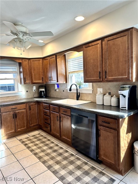 kitchen featuring dark countertops, backsplash, black dishwasher, light tile patterned floors, and a sink