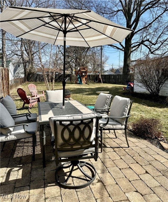 view of patio with outdoor dining area, a playground, and a fenced backyard