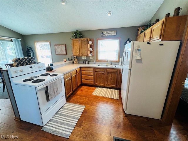 kitchen with light countertops, a peninsula, wood finished floors, white appliances, and a sink