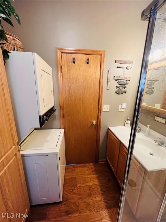 clothes washing area featuring a sink, dark wood-type flooring, stacked washer and clothes dryer, and laundry area