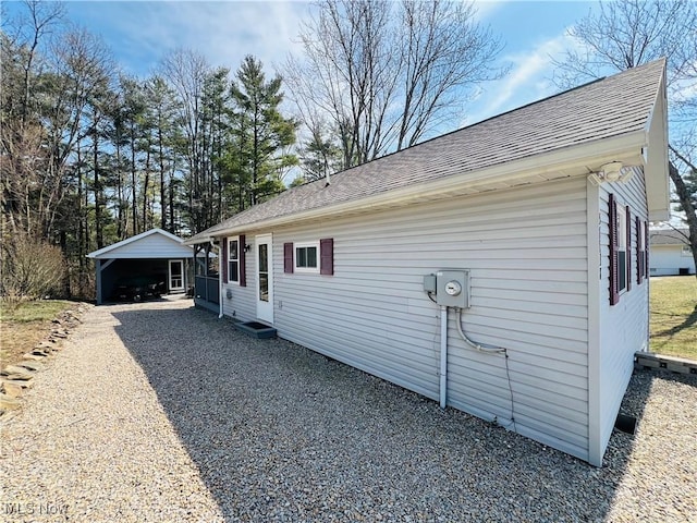 view of property exterior with gravel driveway, a carport, and roof with shingles