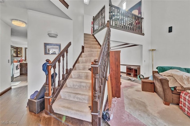 staircase featuring a high ceiling, baseboards, and wood finished floors