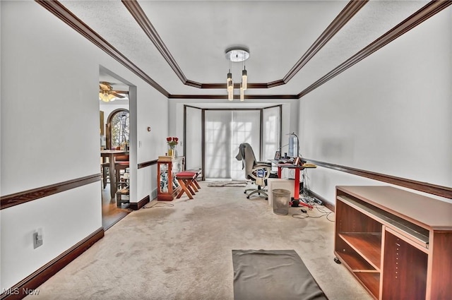 interior space featuring a raised ceiling, carpet flooring, crown molding, baseboards, and ceiling fan