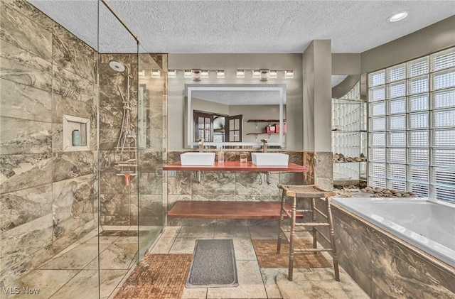 bathroom featuring double vanity, a tile shower, a sink, a textured ceiling, and a garden tub