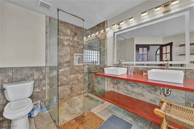 full bathroom with visible vents, a textured ceiling, tile walls, and a sink