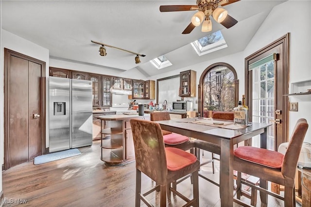 dining space featuring vaulted ceiling with skylight, track lighting, a ceiling fan, and light wood finished floors