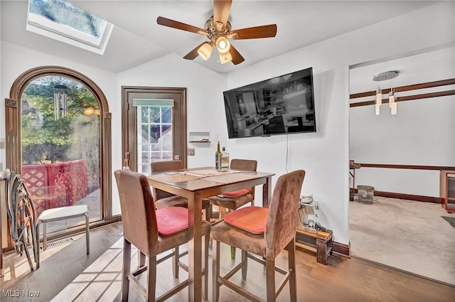 dining area featuring lofted ceiling with skylight, baseboards, ceiling fan, and wood finished floors