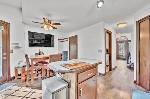 kitchen featuring light wood-style flooring, ceiling fan with notable chandelier, and baseboards