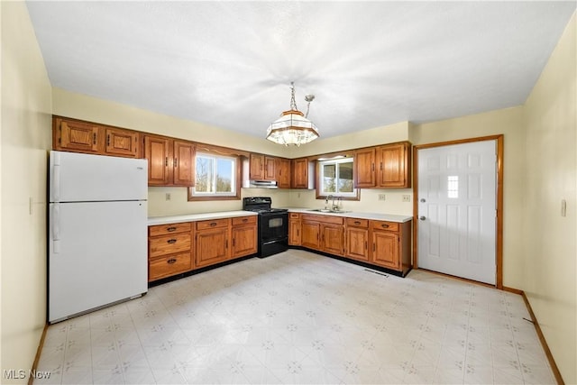 kitchen featuring brown cabinetry, light floors, electric range, freestanding refrigerator, and a sink