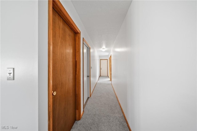 hallway featuring baseboards and light colored carpet