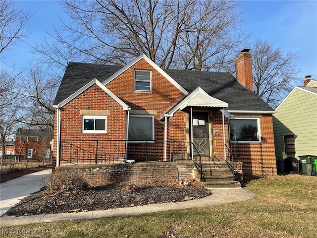 bungalow-style home with brick siding, a chimney, a shingled roof, and a front yard