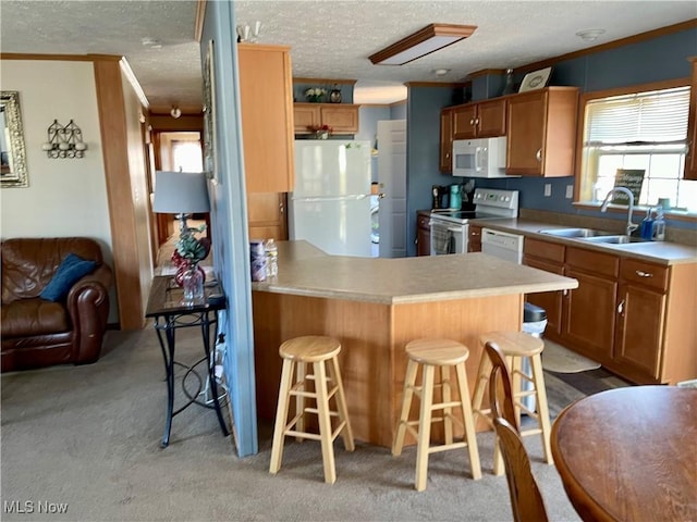 kitchen featuring light colored carpet, a peninsula, a kitchen breakfast bar, white appliances, and a sink